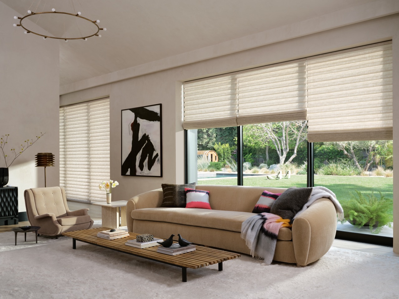 Vignette® Modern Roman Shades across a bright living room with layered cream fabric folds and expansive garden views