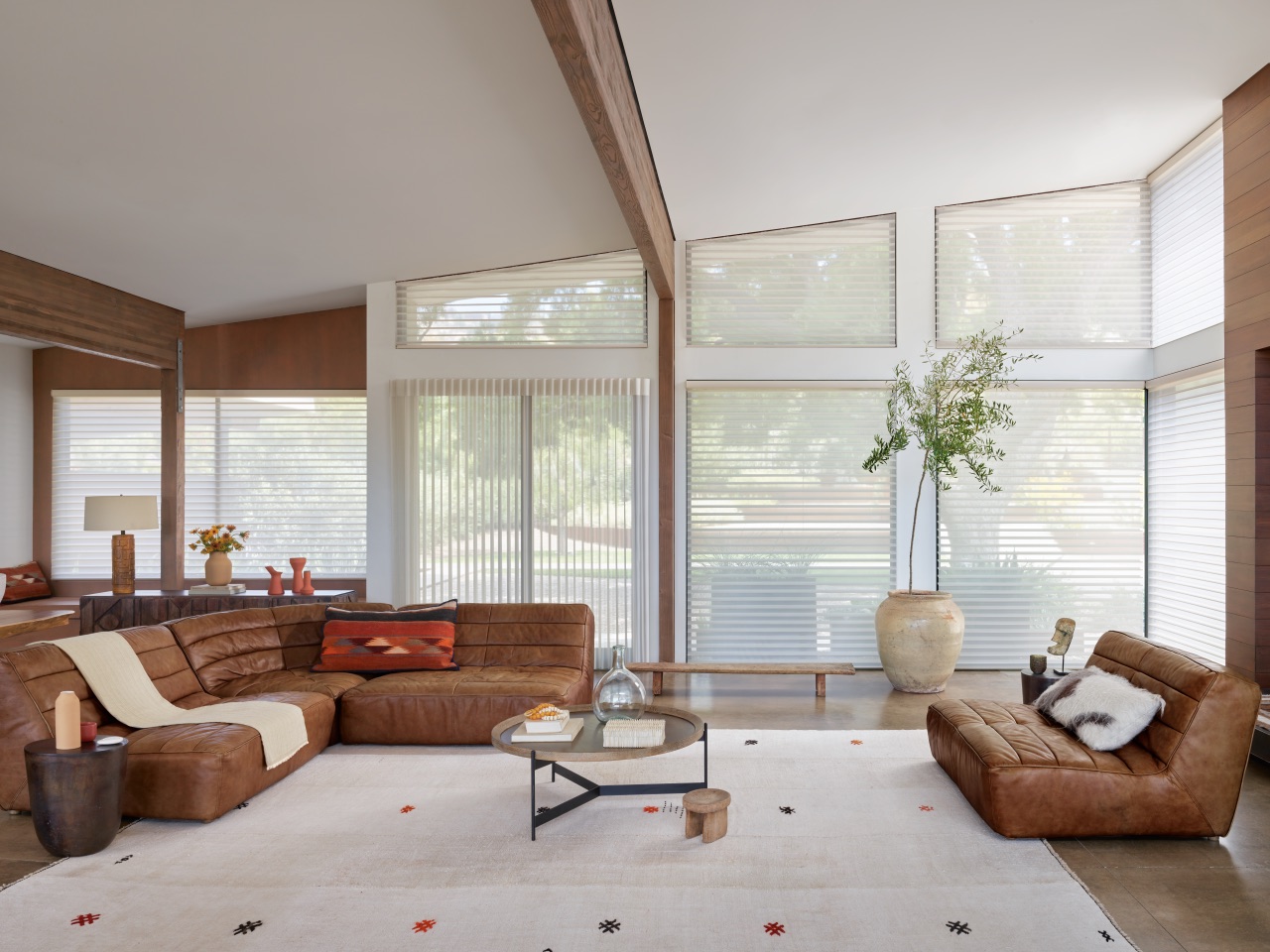 Silhouette® Window Shadings beside Luminette® Privacy Sheers in a warm living room with tall glass and filtered daylight