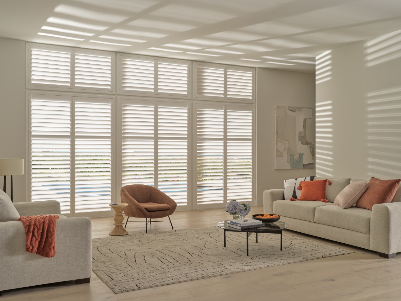 Palm Beach™ Polysatin™ Shutters spanning a bright living room with broad custom-fitted white panels and soft afternoon light